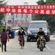 Residents pass under banners which reads "Obeying the law is every citizen's duty and responsibility" and "Recognize the truth, insist on separating from unlawful members" at the entrance to Dongzhou village near Shanwei, Guangdong, Southern China, Wednesday, Dec. 14, 2005.